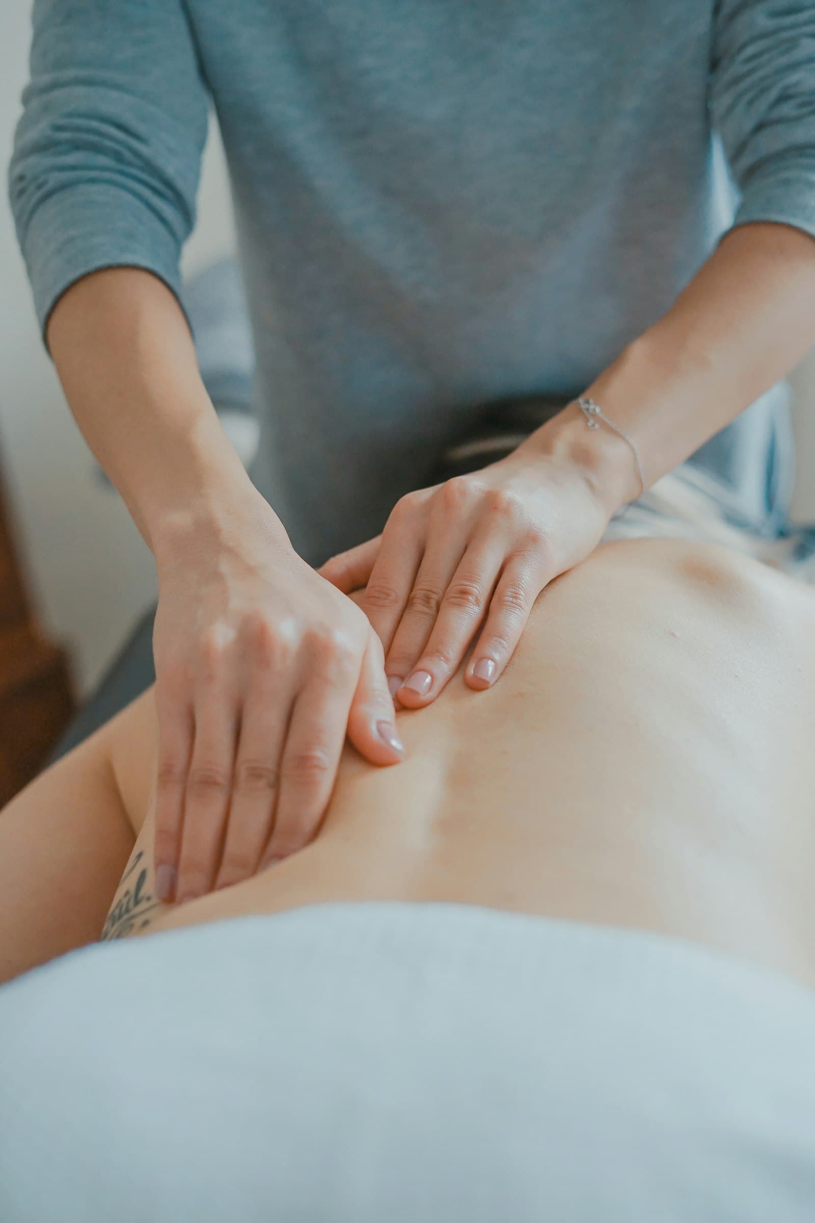 A practitioner's hands easing tension along a patient's lower back during a manual therapy session